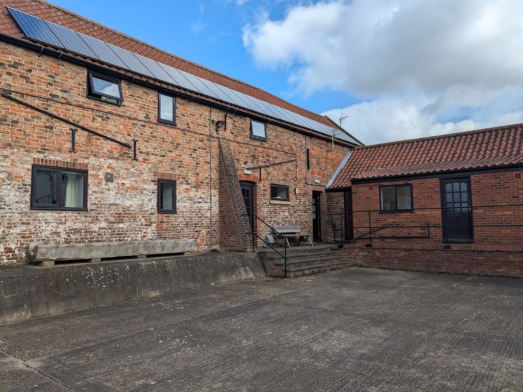Brick buildings with solar panels, a staircase, and a courtyard under a blue sky with clouds at Highfield Farm Campsite.