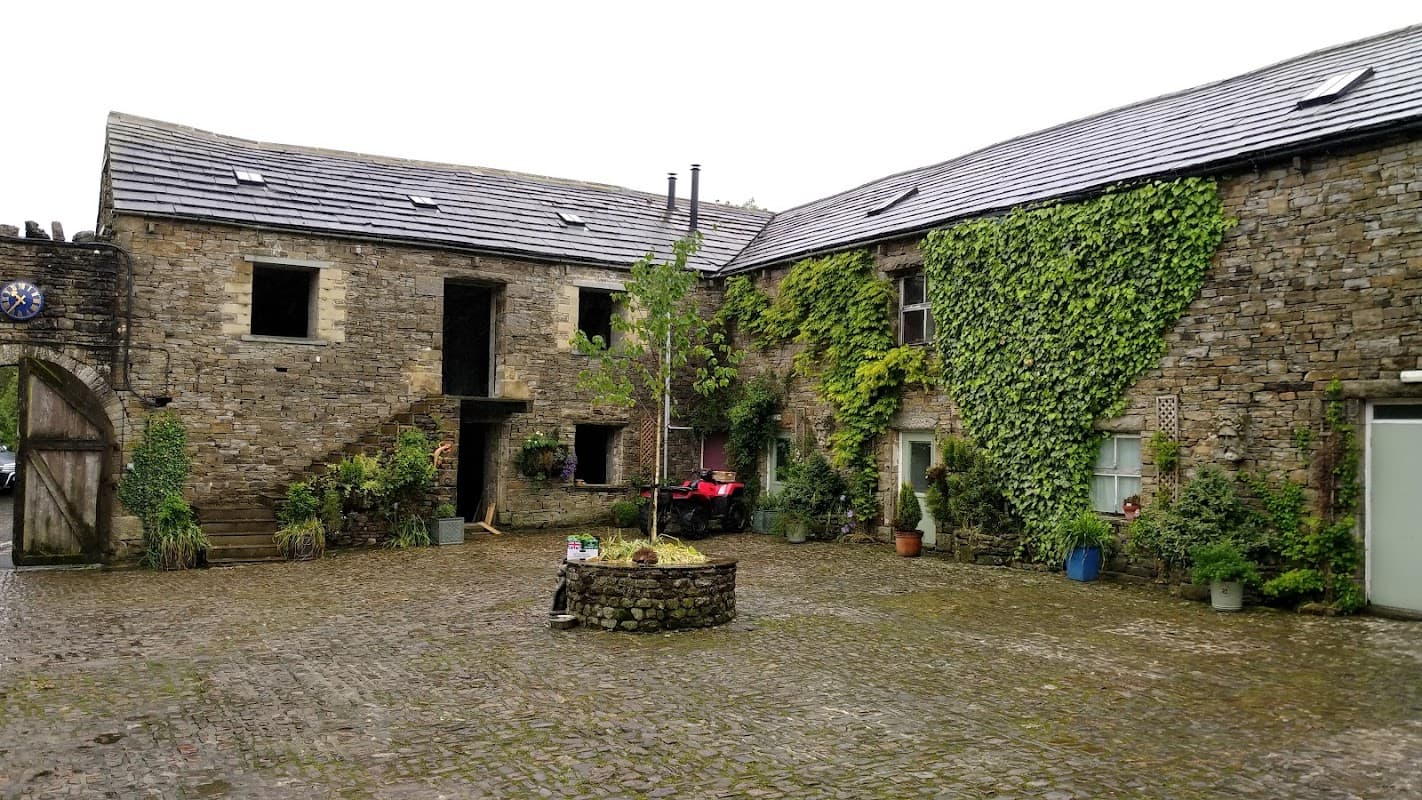Stone buildings with ivy-covered walls, a central stone planter, and a cobblestone courtyard in a rural setting.