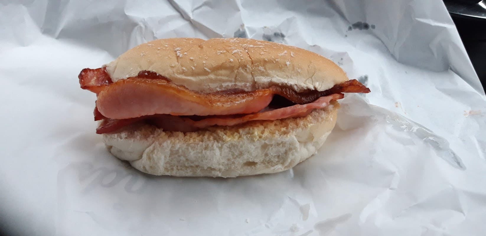 Bacon sandwich on a soft bun, resting on crumpled white paper.