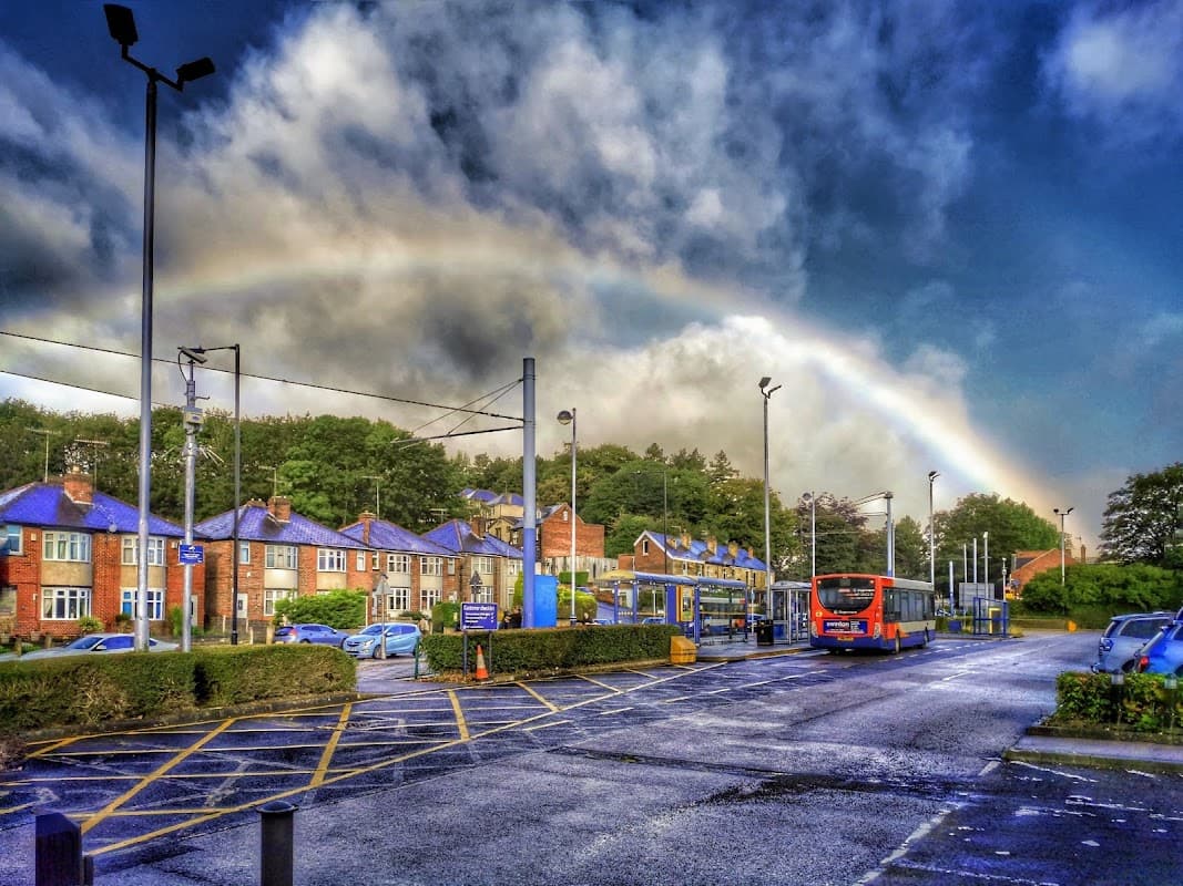 Free parking area at Middlewood Park & Ride, with a rainbow and cloudy sky above, surrounded by greenery and buildings.