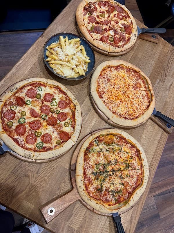 Four pizzas on wooden boards with a bowl of fries, set on a wooden table in a cozy bar environment.