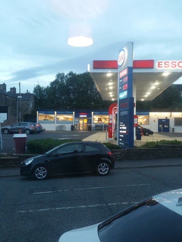 Tesco Esso Express shop with fuel pumps, parked cars, and a cloudy evening sky in Ovenden, Yorkshire.