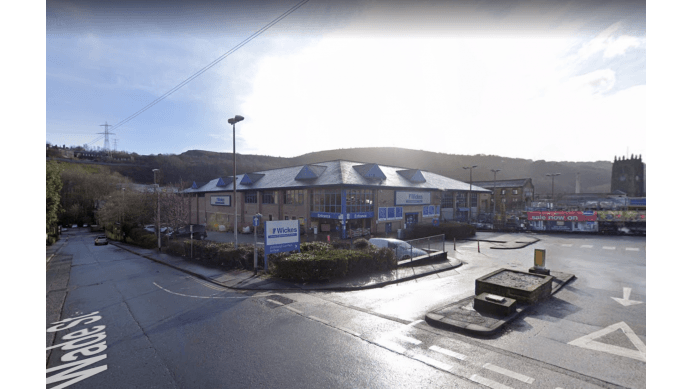 Pay & Display parking area in Ovenden, Yorkshire, with a building and hills in the background under a bright sky.