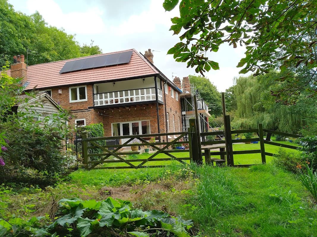 A charming brick house with solar panels, surrounded by greenery and a wooden fence in Over Dinsdale, Yorkshire.