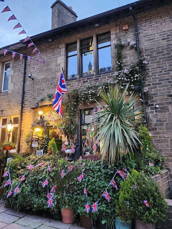 Charming hotel with British flags, greenery, and flower pots, set in a stone building in Oxenhope, Yorkshire.