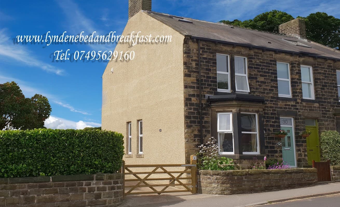 Charming stone guest house with green door, hedges, and flowers in Penistone, Yorkshire, under a blue sky.
