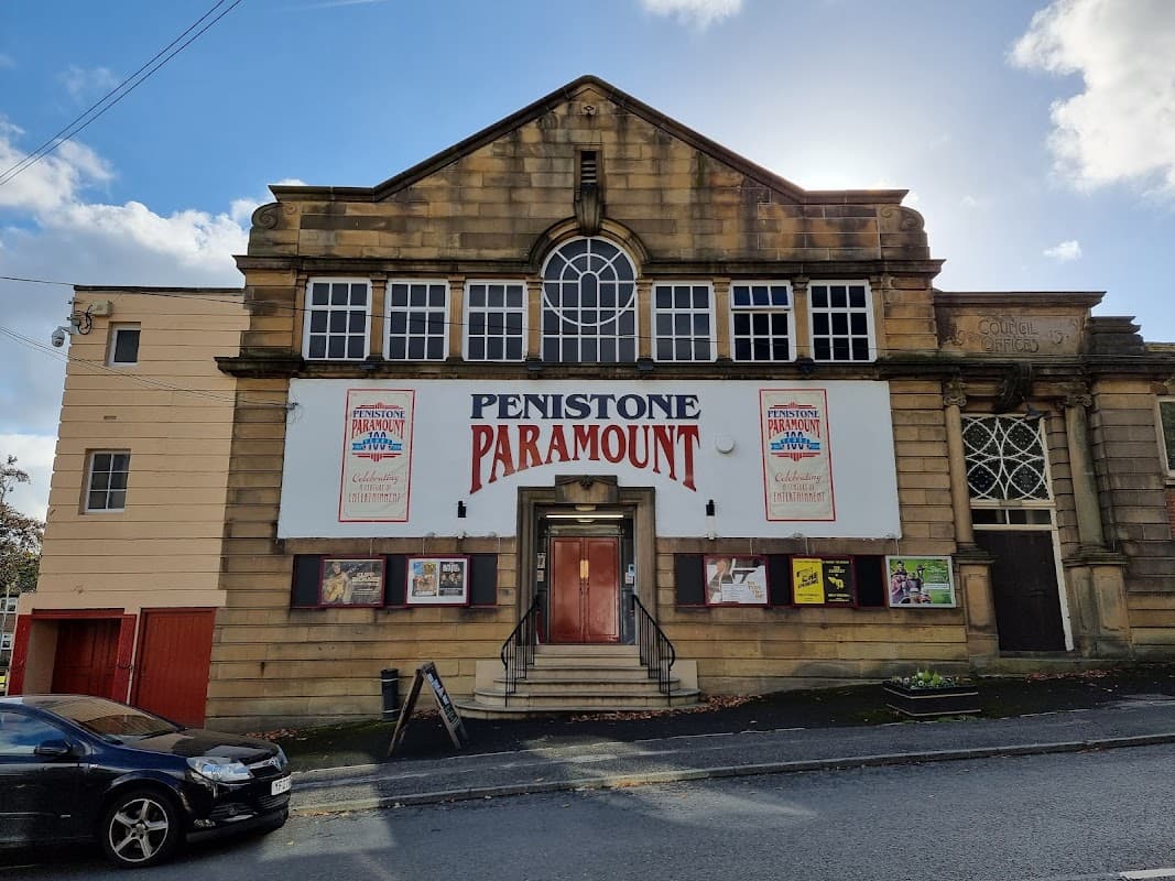 Historic cinema building with large "Penistone Paramount" sign, decorative stonework, and a blue sky backdrop.