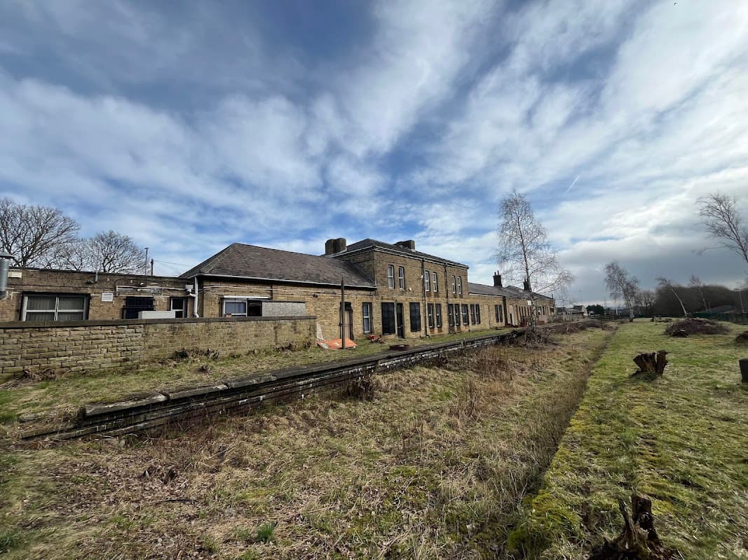 Historic railway station building with stone facade, overgrown tracks, and a cloudy sky in Penistone, Yorkshire.