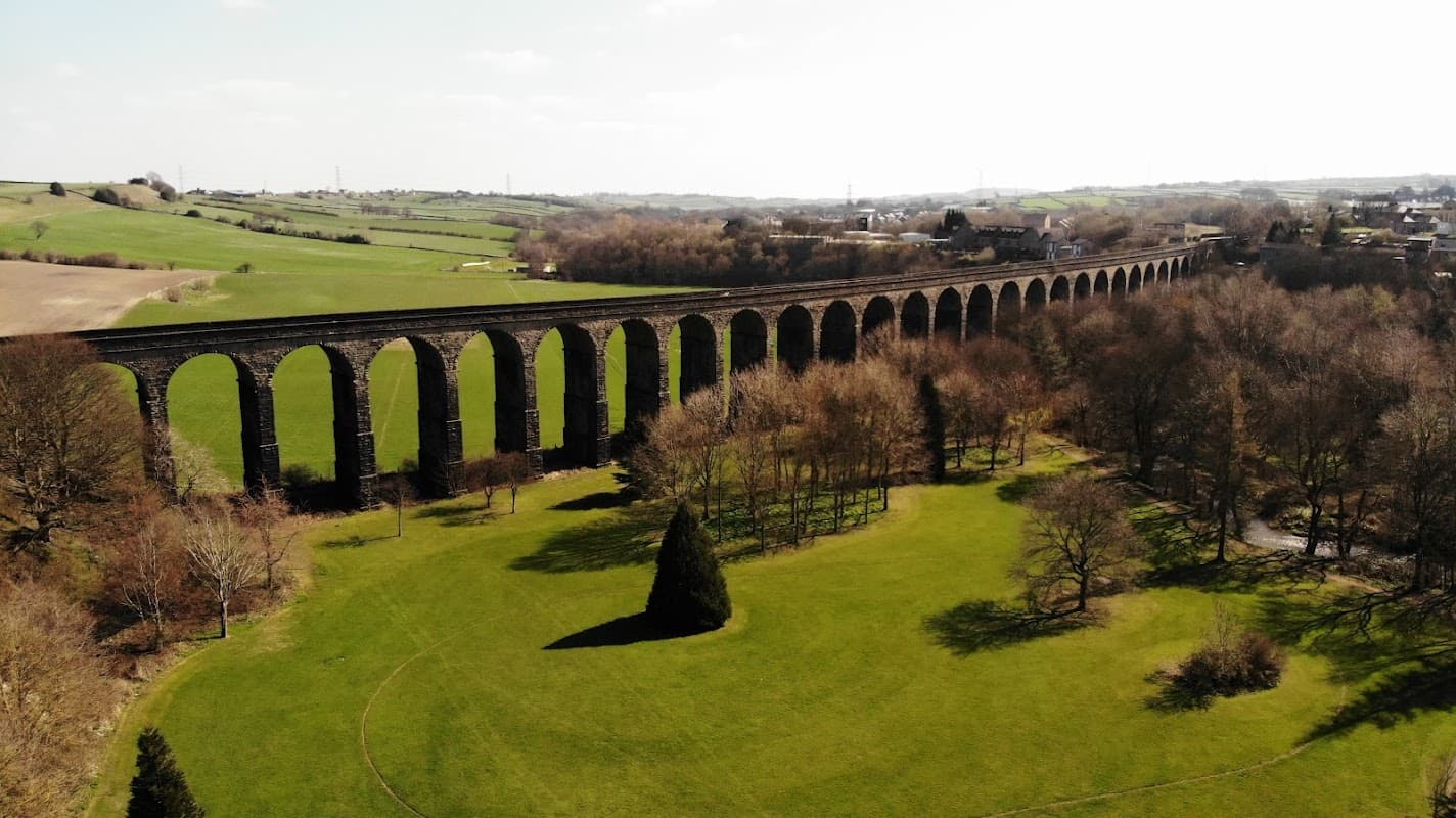 Aerial view of Watermeadows Park featuring a large stone viaduct and lush green fields under a clear sky.