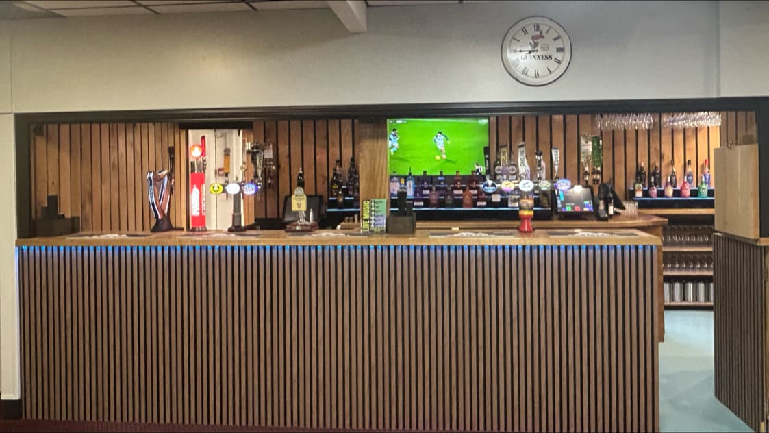 Wooden bar with various drink taps, a TV showing sports, and a clock on the wall at Pickering Recreation Club.