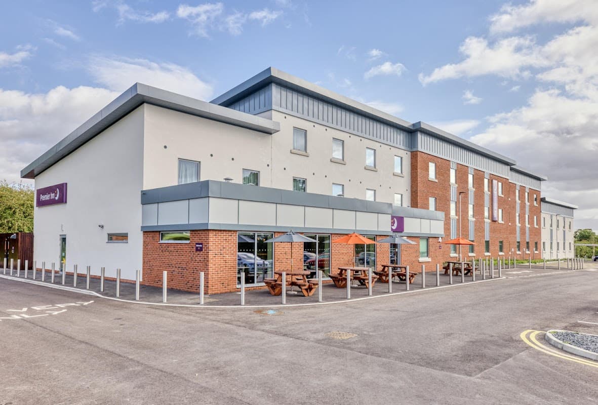 Modern hotel building with a mix of brick and white exterior, outdoor seating with orange umbrellas, and clear blue sky.