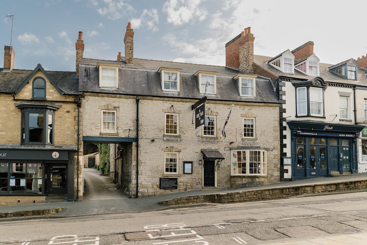 Historic stone building with a black sign, surrounded by other shops and a blue sky in Pickering, Yorkshire.