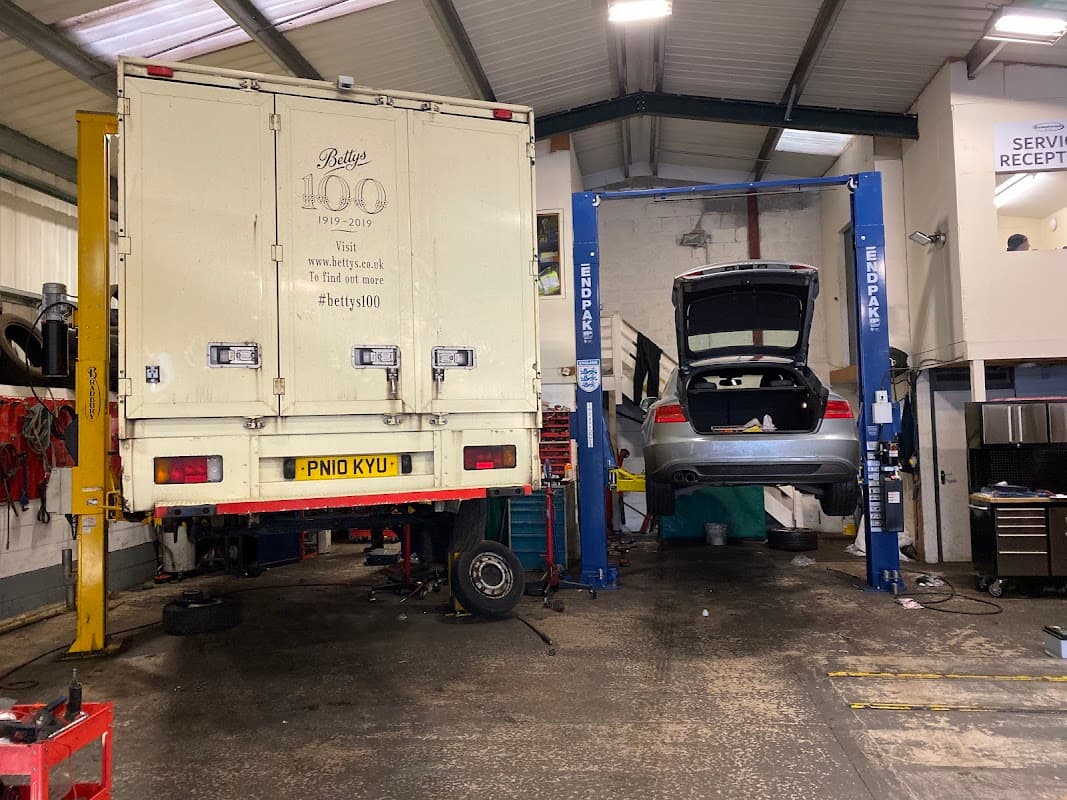 Two vehicles on lifts in a garage, one a truck and the other a car, with tools and equipment visible in the background.