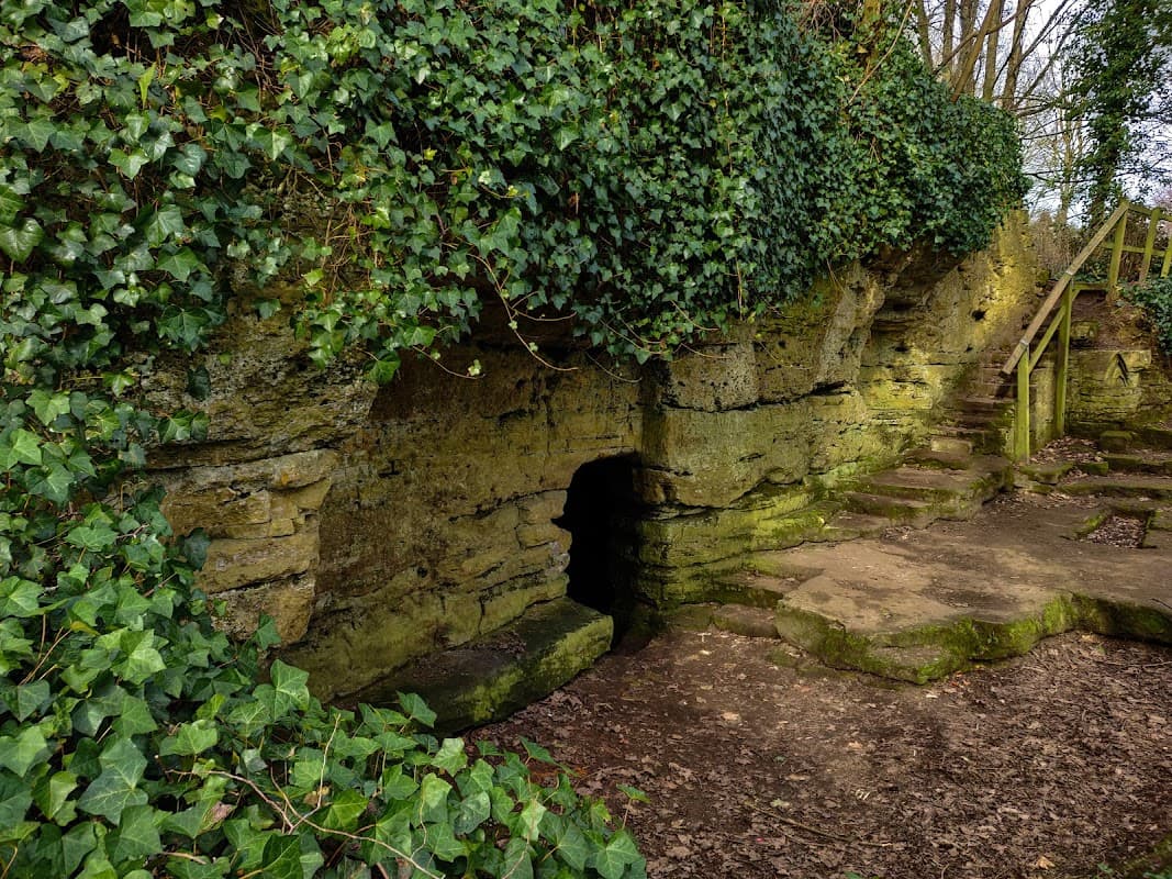 St Robert's Cave features a stone entrance surrounded by lush greenery and steps leading up the hillside.