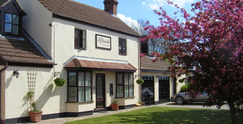 Charming two-story guest house with a sign, surrounded by greenery and blooming pink flowers in Pollington, Yorkshire.