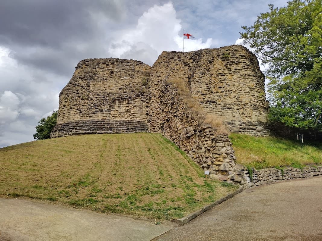 Pontefract Castle ruins with grassy slopes and a flag atop, under a cloudy sky in Yorkshire. Free parking nearby.