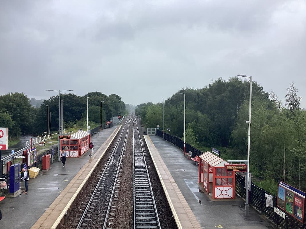 Bus stops with red shelters along a railway track, surrounded by trees under a cloudy sky in Pontefract, Yorkshire.