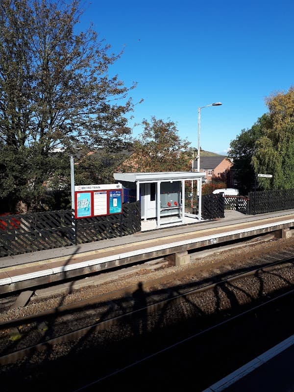 Bus stop at Pontefract Tanshelf with a clear blue sky, trees, and a nearby fence along the railway tracks.