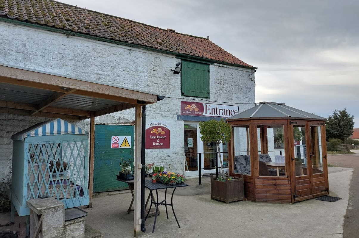 Quaint stone building with green door, sign for bakery, and outdoor seating area with flowers in Potter Brompton, Yorkshire.