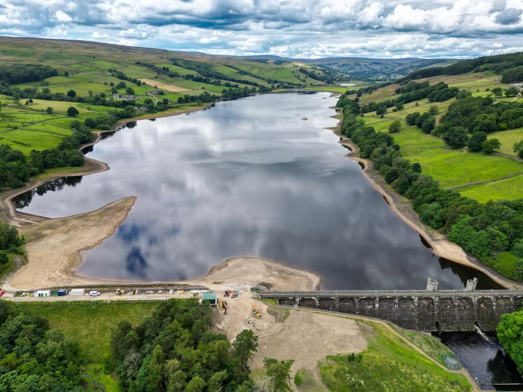 Aerial view of Gouthwaite Reservoir with calm waters, green hills, and a dam structure along the shoreline.