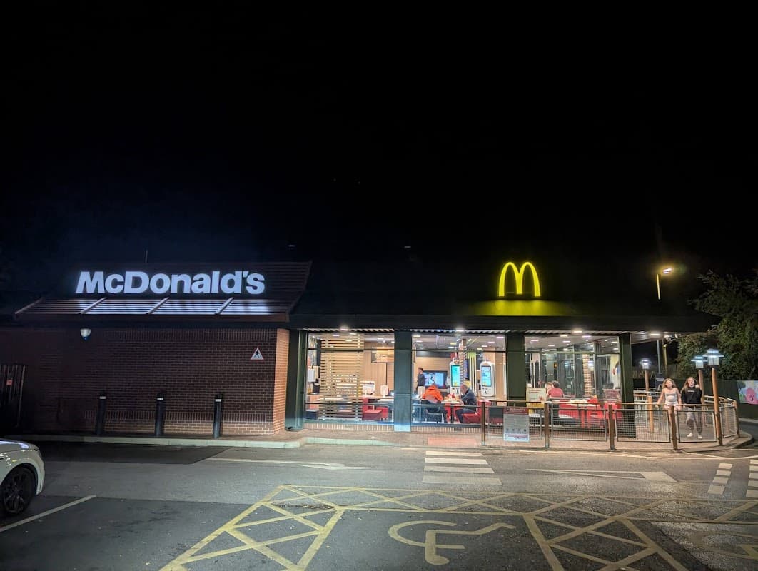 McDonald's restaurant at night, featuring a bright yellow logo and illuminated dining area with customers inside.