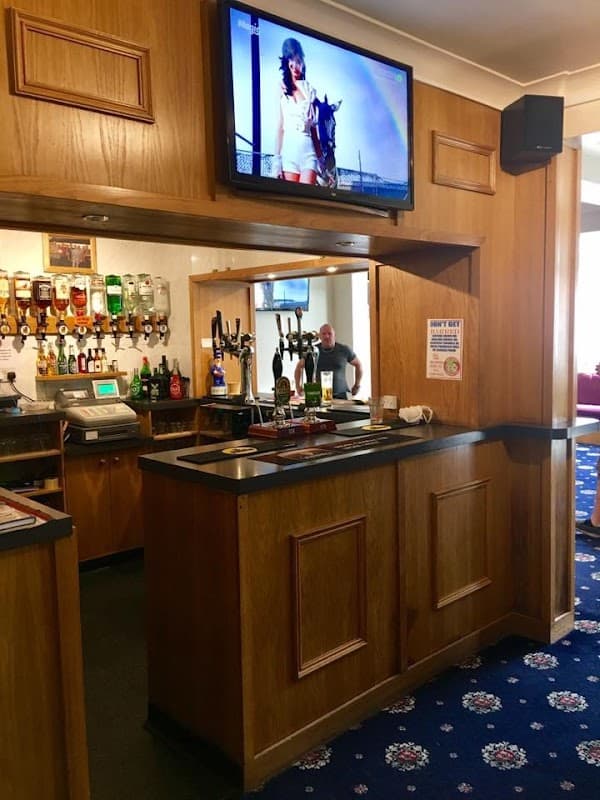 Wooden bar with drinks, a TV on the wall, and a person in the background at Rawcliffe Bridge Club.
