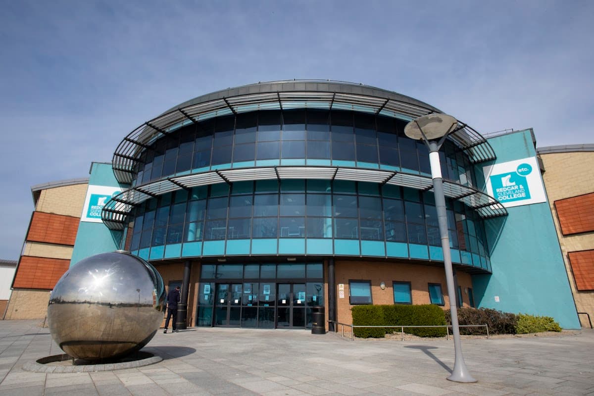 Modern college building with large glass windows, blue accents, and a reflective sculpture in the foreground.