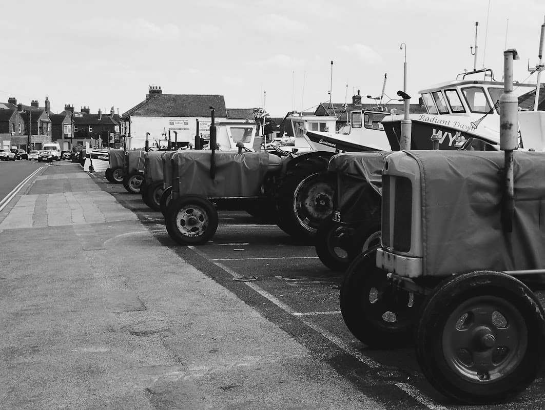 Row of covered tractors parked in Fishermans Square Car Park, with boats and buildings in the background.