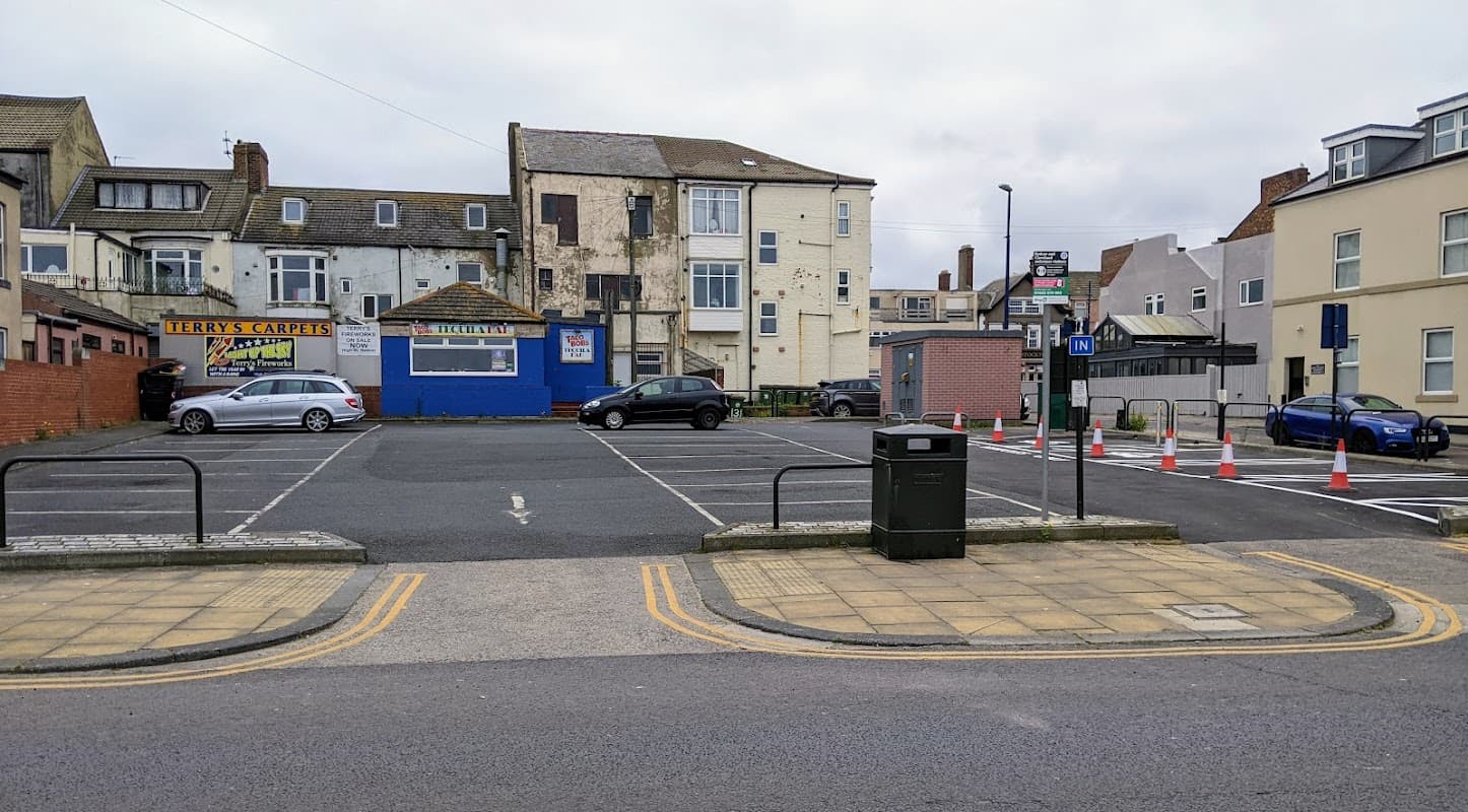 Pay & Display car park with empty spaces, nearby buildings, a signpost, and a trash bin in Redcar and Cleveland.