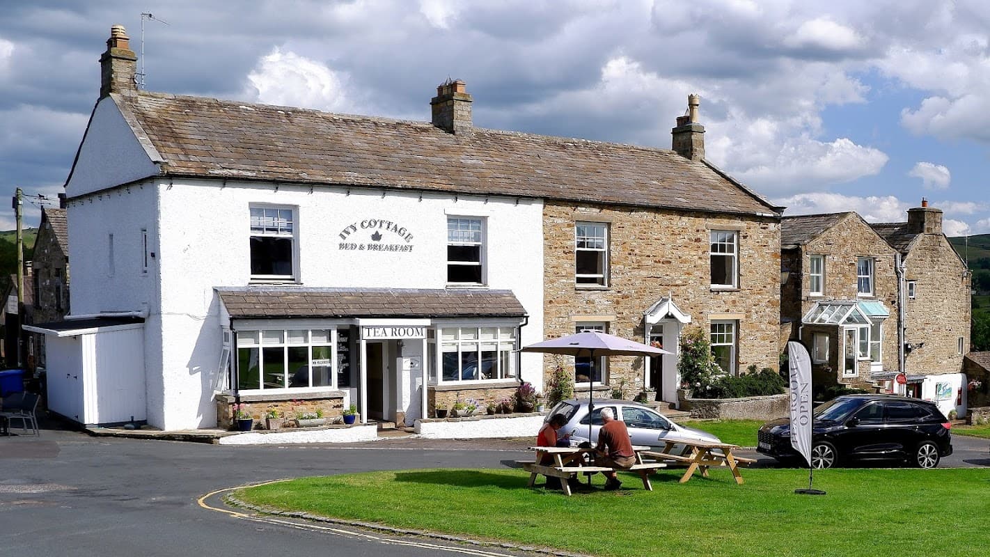 Ivy Cottage Bed & Breakfast with outdoor seating, a tea room sign, and stone buildings under a cloudy sky in Reeth.
