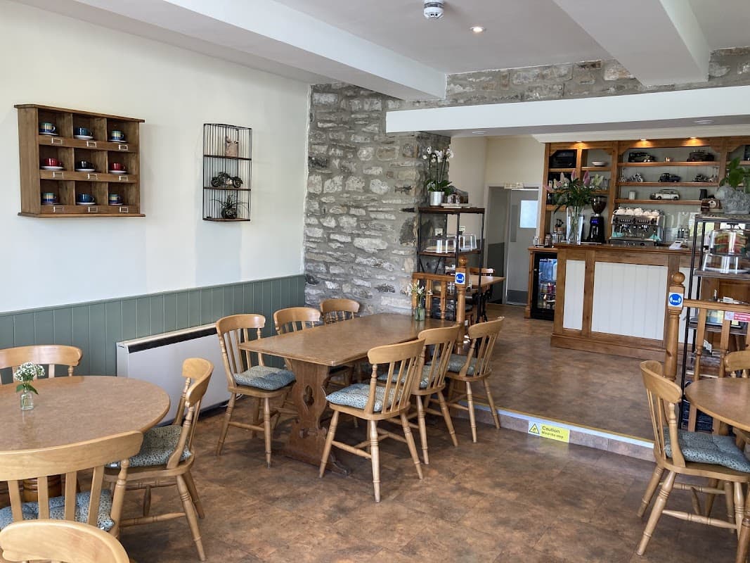 Cozy café interior with wooden tables, chairs, stone walls, and a counter adorned with plants and displays.