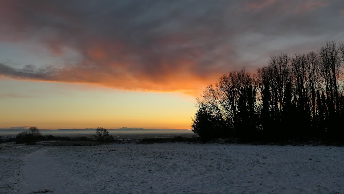 Sunset over snow-covered ground with silhouetted trees and a colorful sky at Richmond Racecourse.