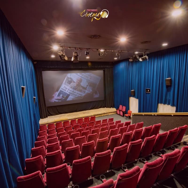 Red velvet seats facing a large screen in a cozy cinema with blue curtains and dim lighting.