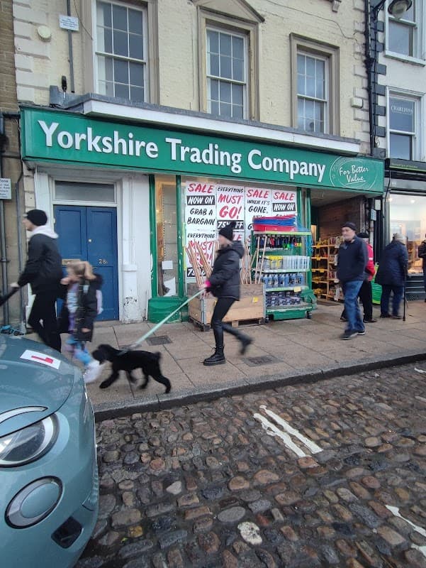 Shopfront of Yorkshire Trading Company in Richmond, with sale signs and people walking by, including a dog.