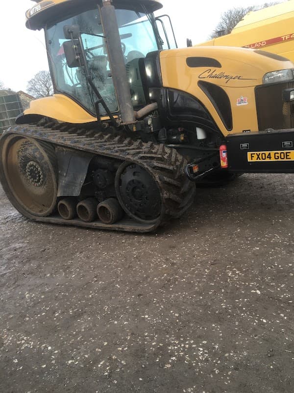 Yellow Challenger tractor with tracks parked on a gravel surface, showing muddy wheels and nearby machinery.