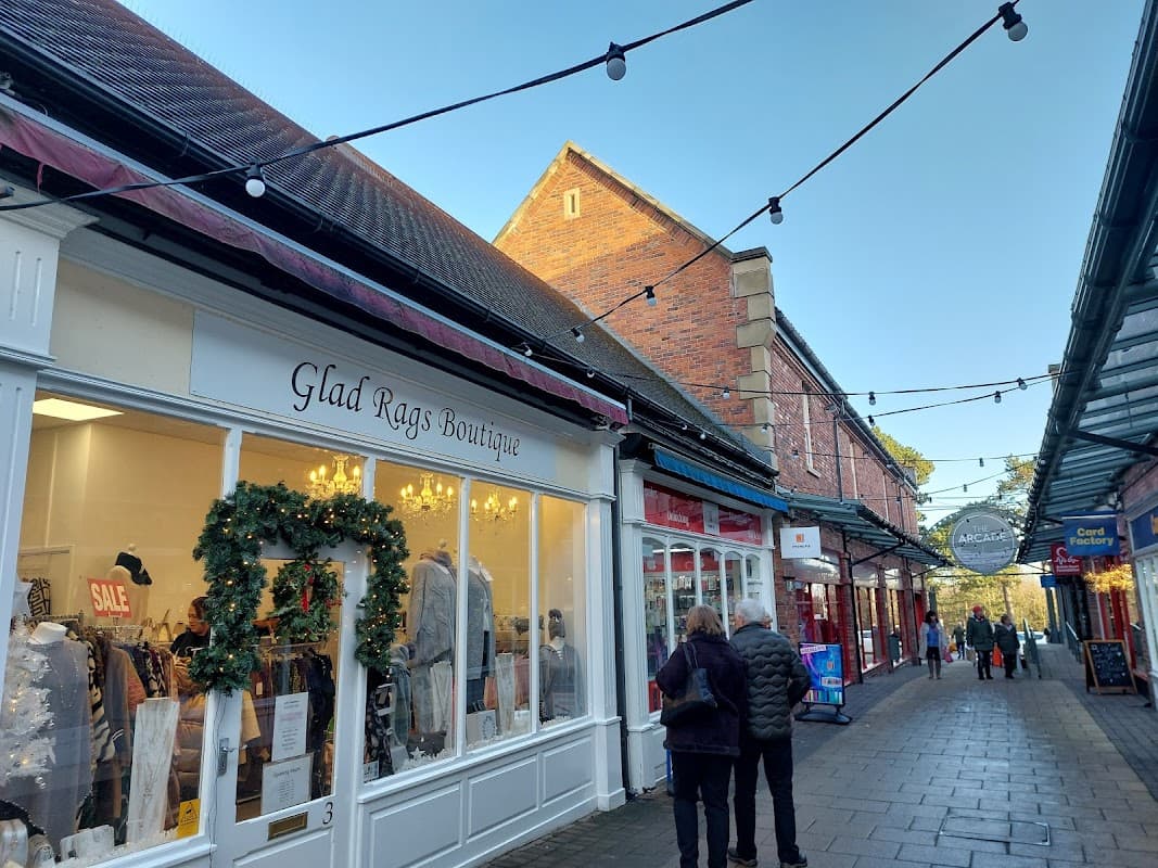 Charming shopping arcade with boutique storefronts, festive decorations, and string lights under a clear blue sky.