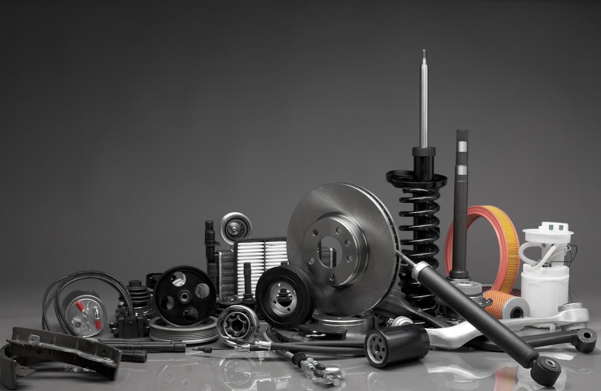 Various automotive parts including brake discs, shock absorbers, filters, and pulleys arranged on a dark background.