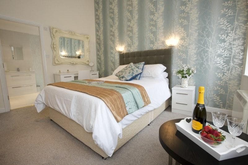 Cozy bedroom with a double bed, light blue floral wallpaper, champagne, strawberries, and elegant decor.