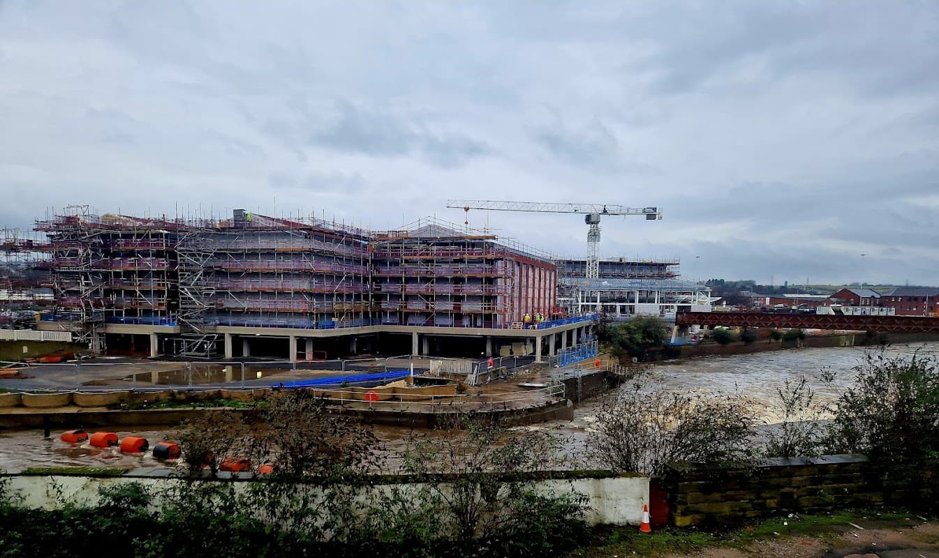 Construction site near a river, with scaffolding, cranes, and a cloudy sky in Rotherham, Yorkshire.