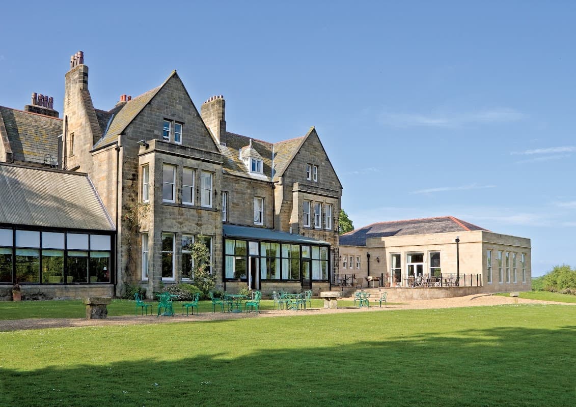 Victorian-style hotel with large windows, green lawn, and outdoor seating against a clear blue sky.