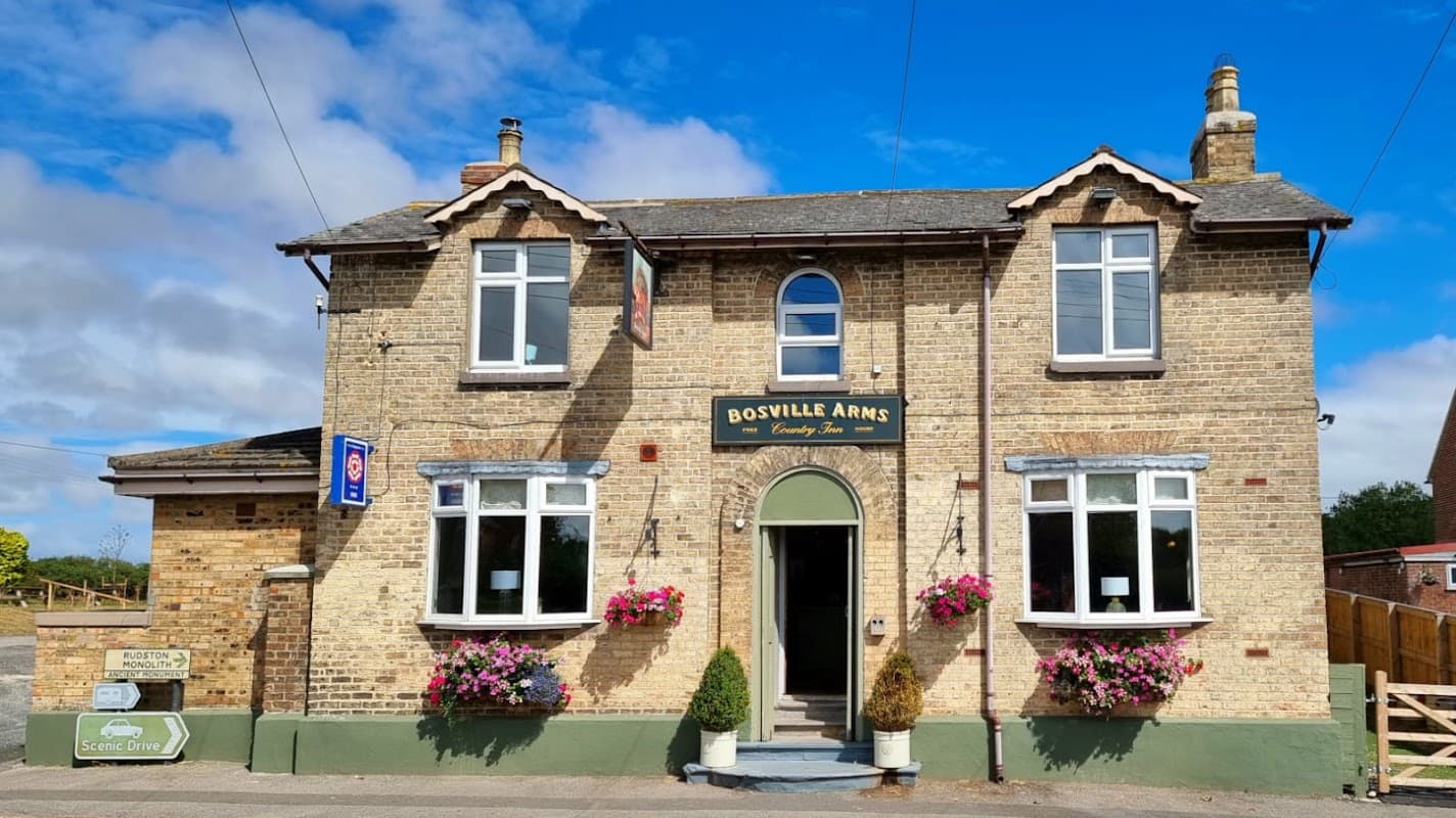 Historic brick hotel with a welcoming entrance, flower baskets, and a clear blue sky in Rudston, Yorkshire.