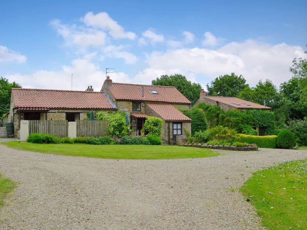Charming stone cottages with red-tiled roofs, set in lush greenery and a gravel driveway in Sawdon, Yorkshire.