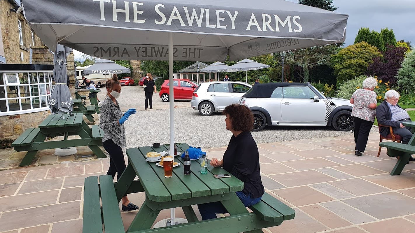 Outdoor dining area at The Sawley Arms with patrons, tables, and a car in the background under a large umbrella.