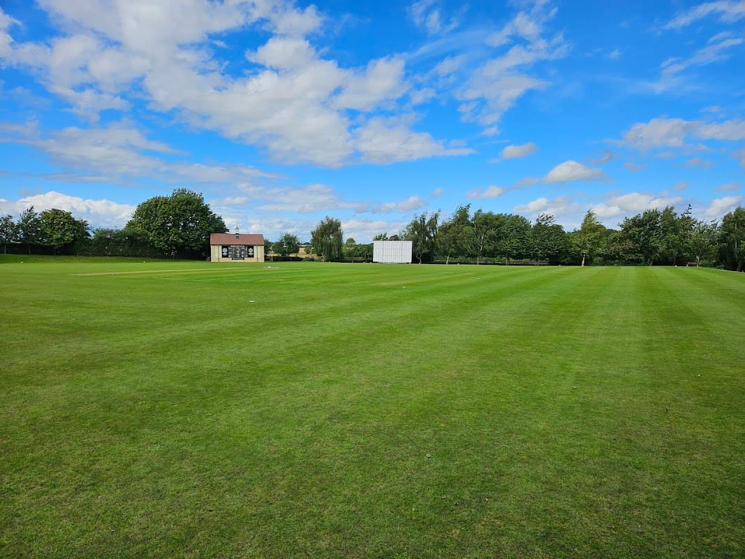 Cricket field with a clubhouse and scoreboard under a blue sky with scattered clouds in Saxton, North Yorkshire.