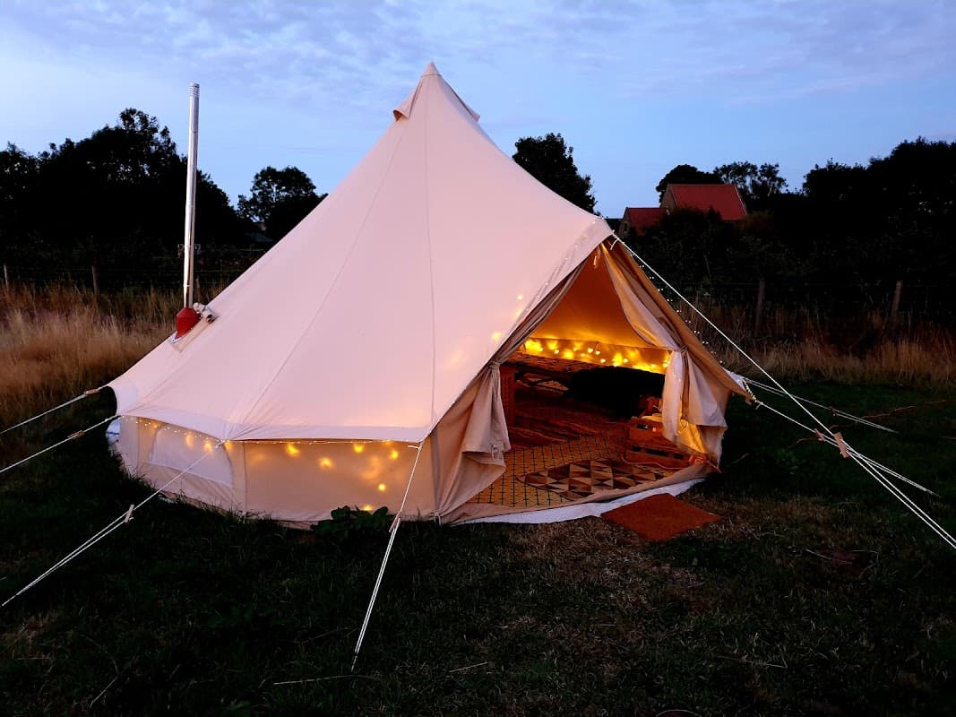 A cozy glamping tent with warm string lights, set in a grassy field at Clover Hill Farm, North Yorkshire.