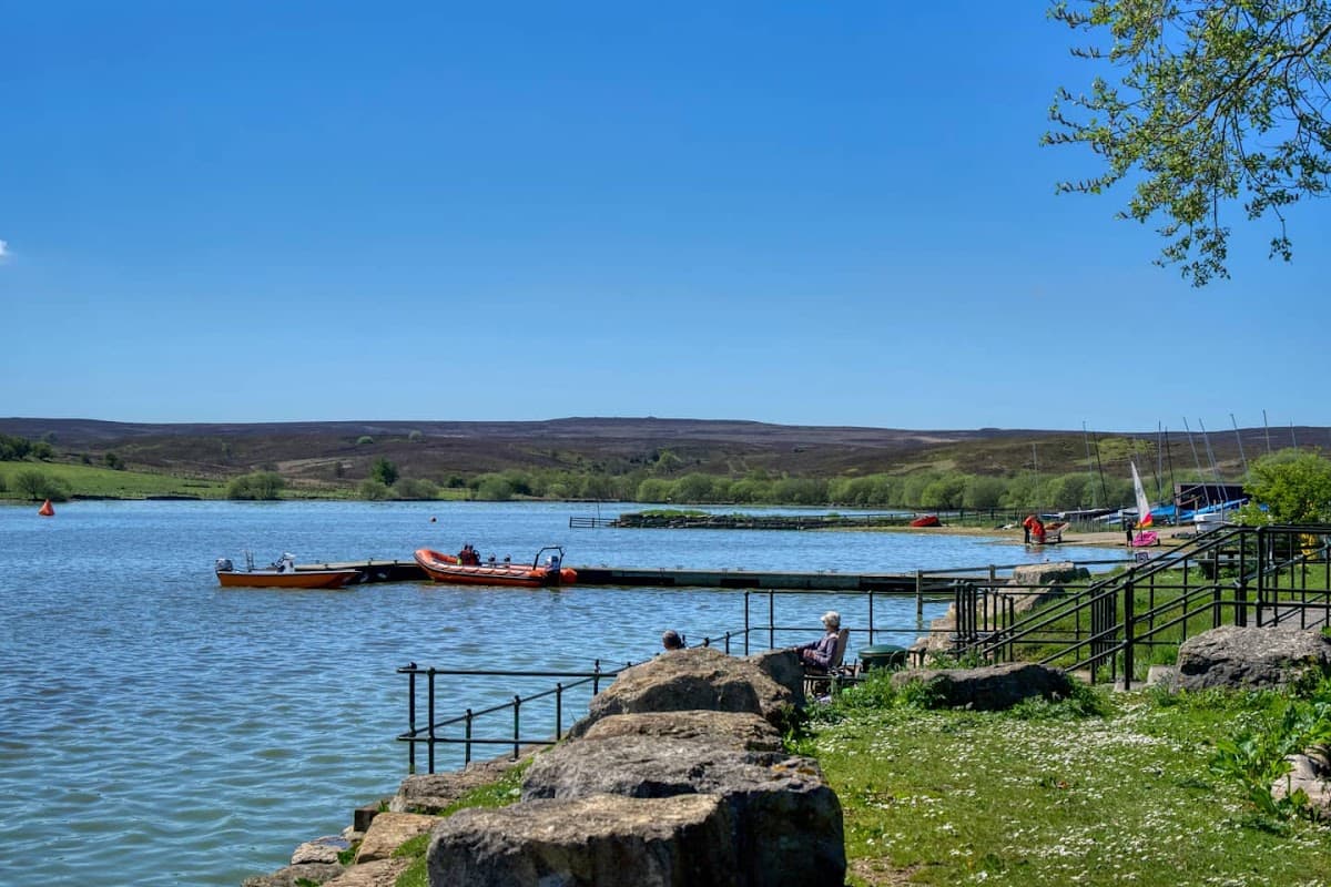 Calm waters of Scaling Dam with boats docked, lush greenery, and a clear blue sky in North Yorkshire.