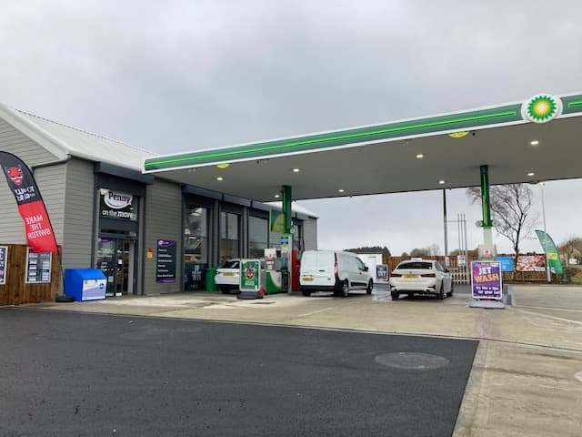 Grocers with a fuel station, featuring a BP sign, cars, and promotional banners in a cloudy setting.