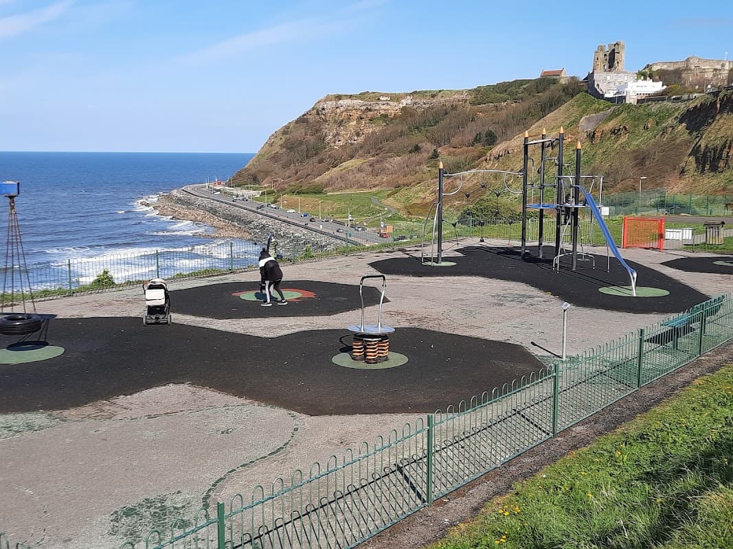 Play park with swings, climbing structures, and a view of the sea and cliffs in Scarborough, Yorkshire.