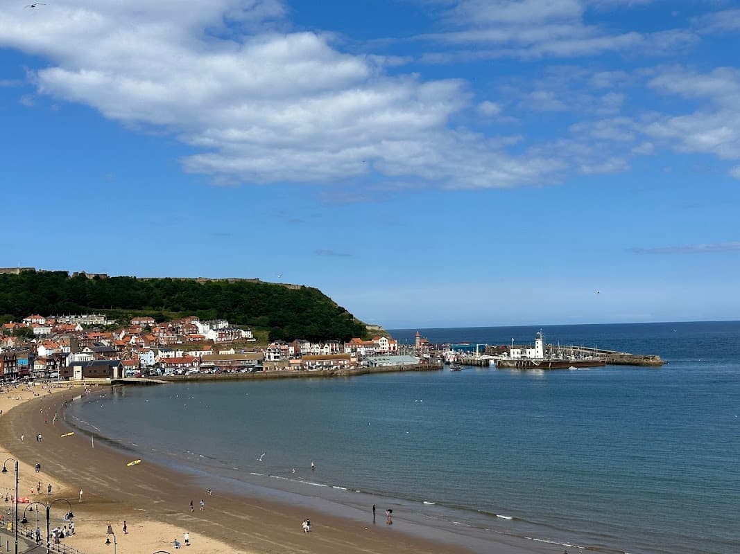 Scarborough's South Bay with sandy beach, colorful buildings, and a pier under a clear blue sky.