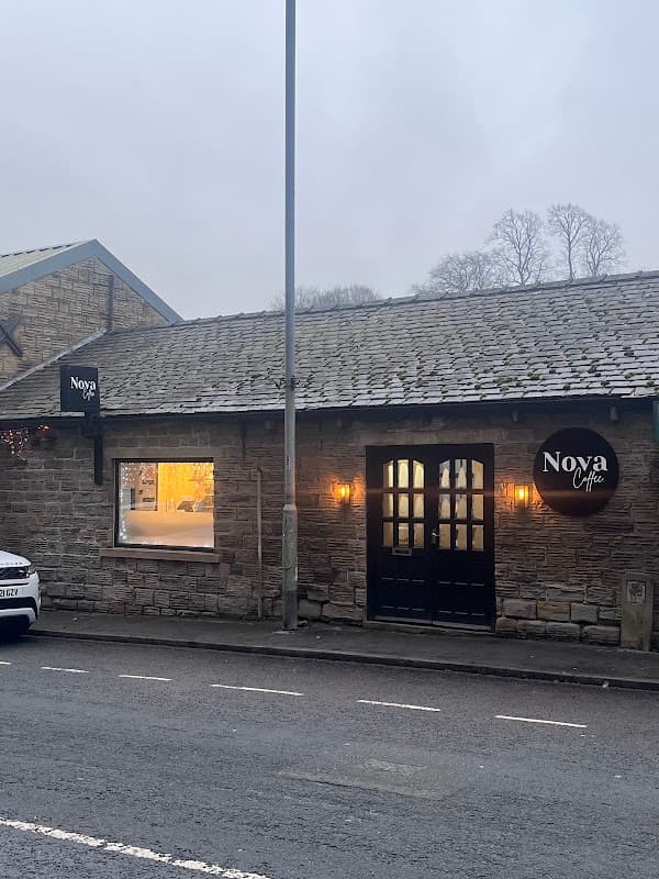 Stone building with a slate roof, featuring large windows, a wooden door, and "Nova Coffee" signage.
